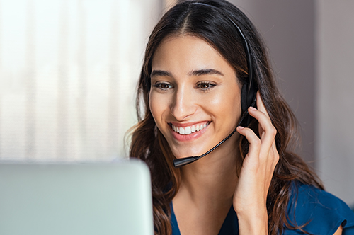 Smiling woman using laptop while talking to customer on phone.